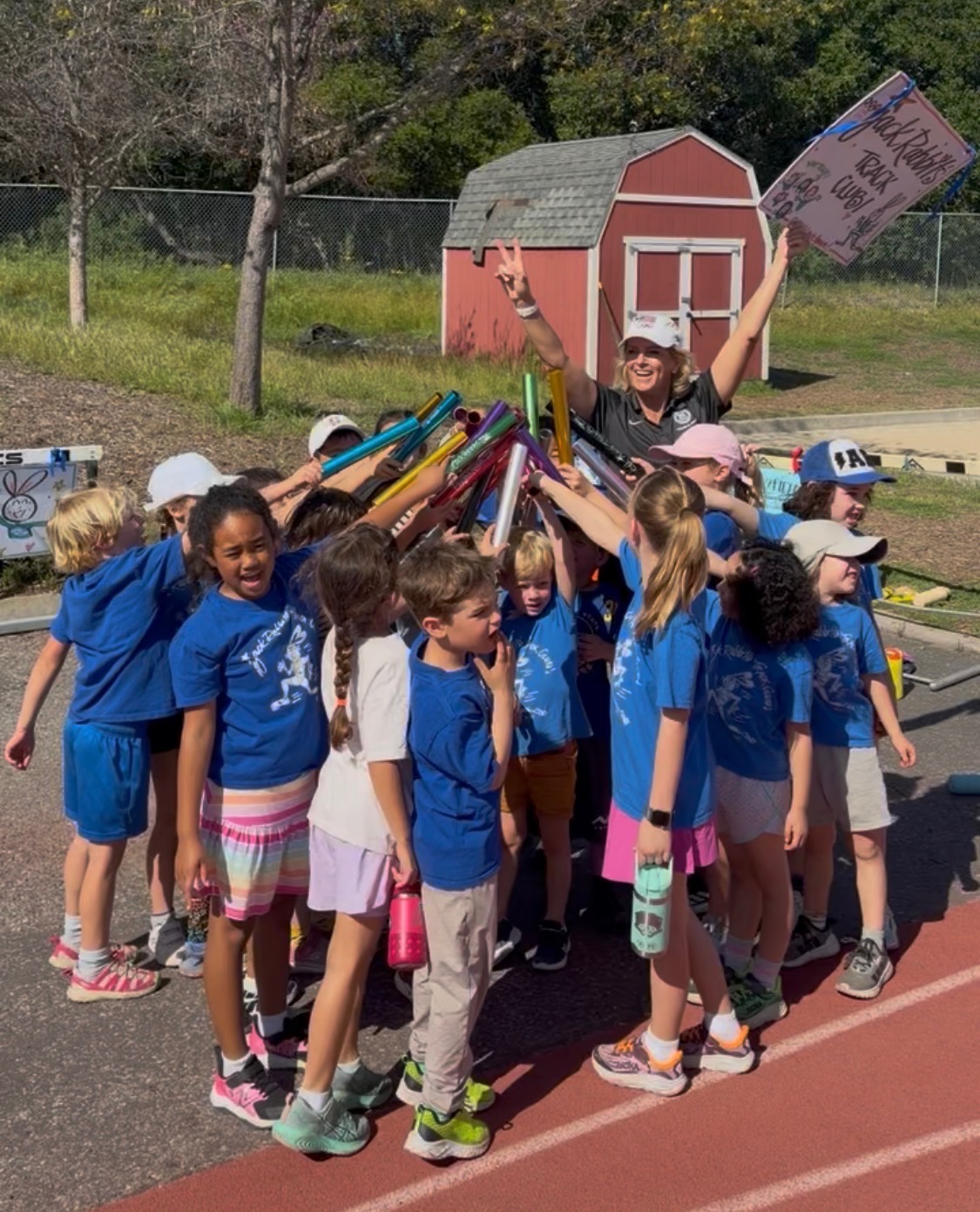 The closing huddle, Joy raising the Jack Rabbits Track Club sign while kids lift their relay batons together