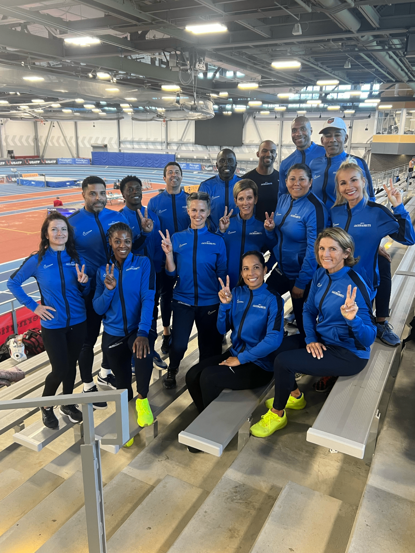 Members of Joys Jackrabbit Masters Track Club smiling together in matching blue team jackets at an indoor track
