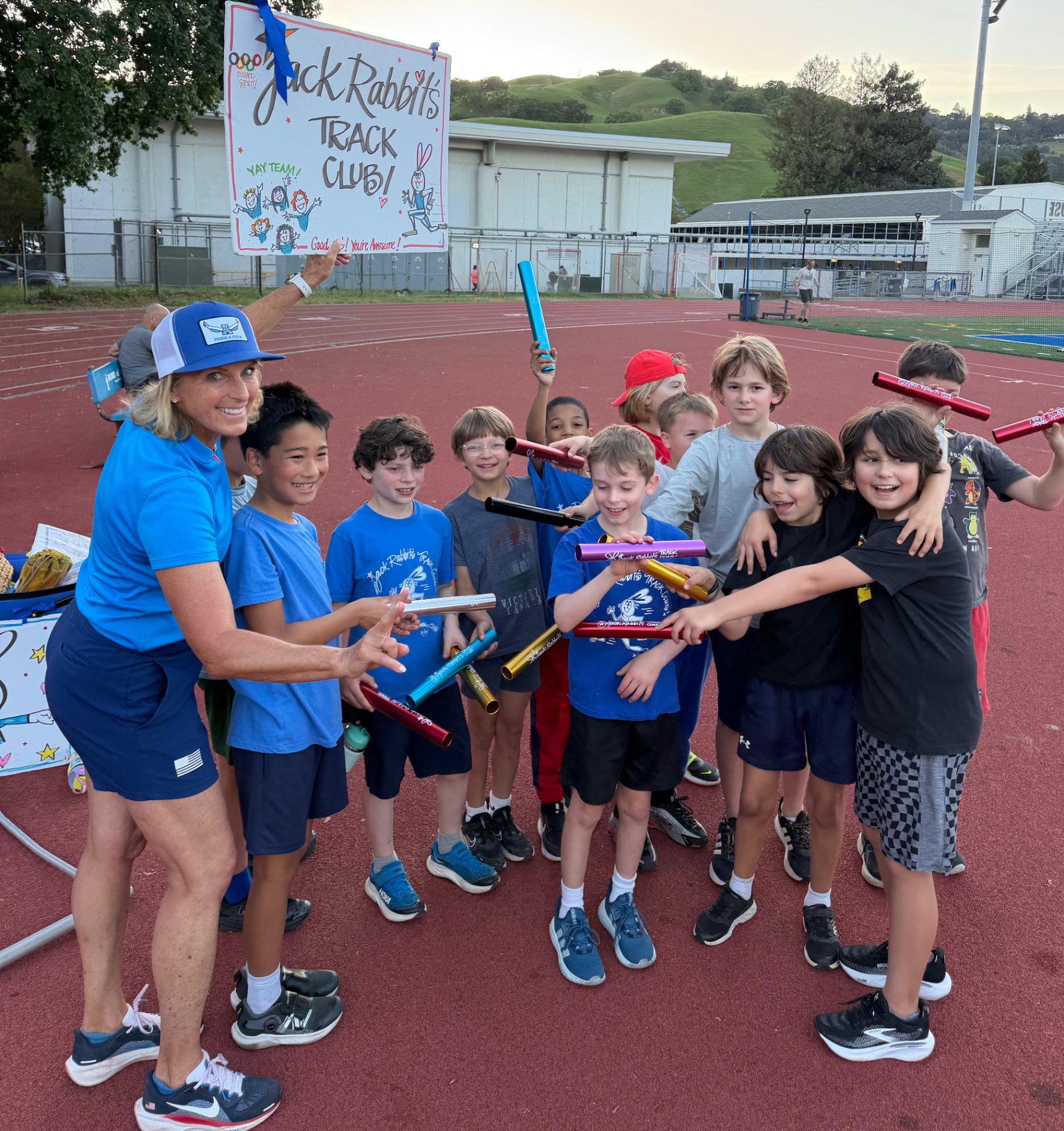 Joy with a Jackrabbits class holding their relay batons beside the club's hand painted sign