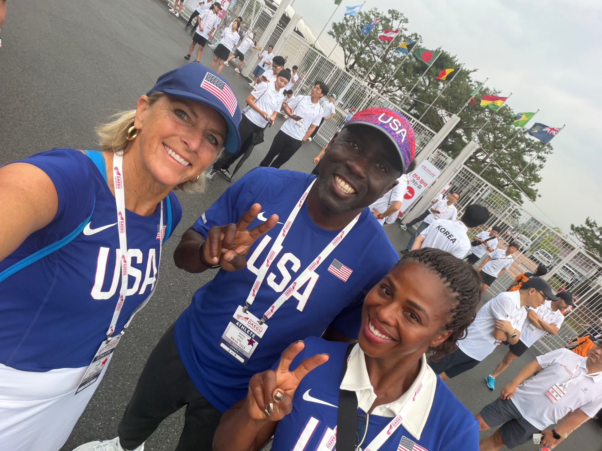 Joy smiling in a Team USA cap and jersey with two members of her Joys Jackrabbit Masters Track Club, all in Team USA gear at the Daegu world championships